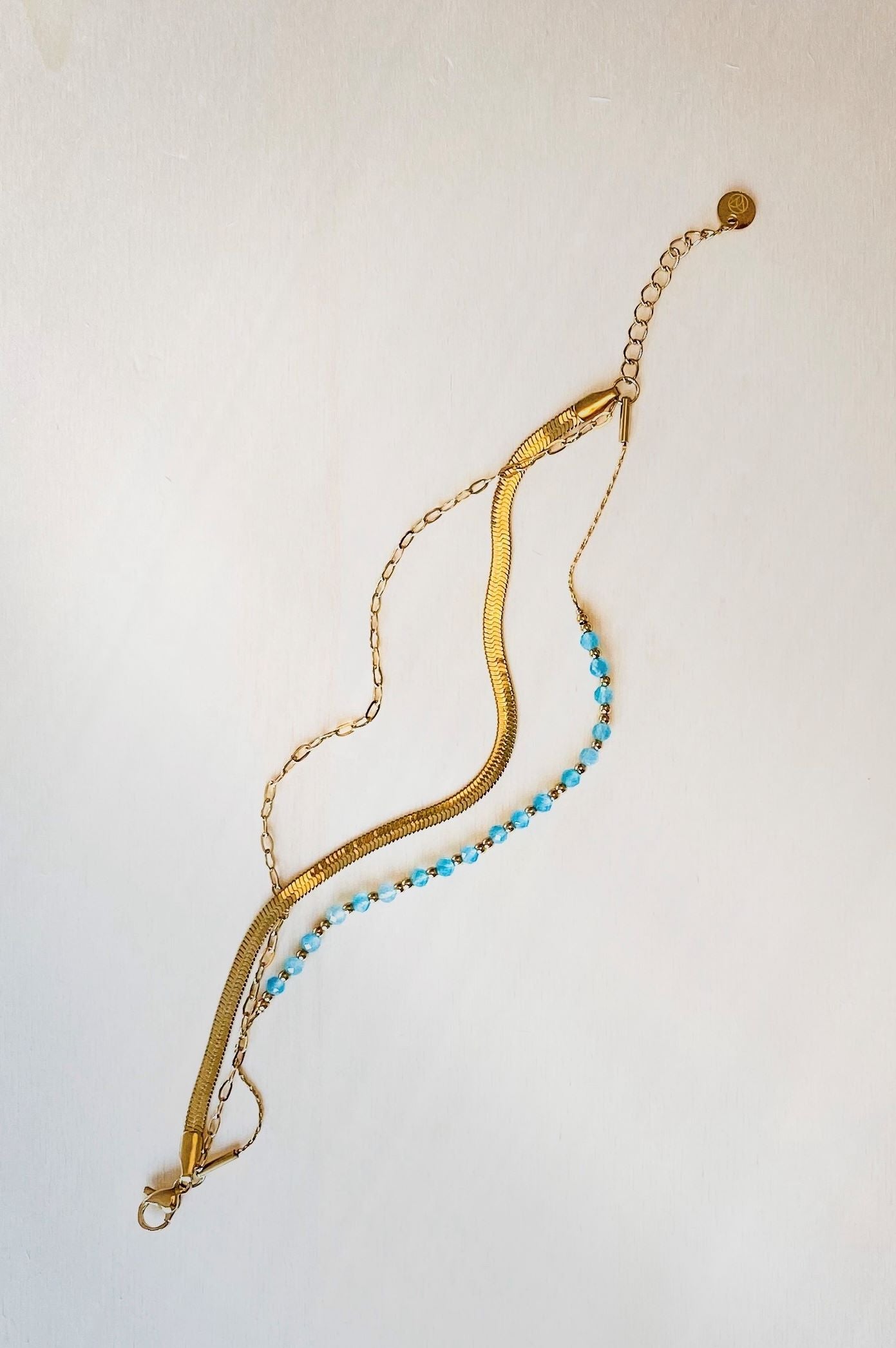 three tier bracelet with snake skin, blue beads and chain element on plain white background.