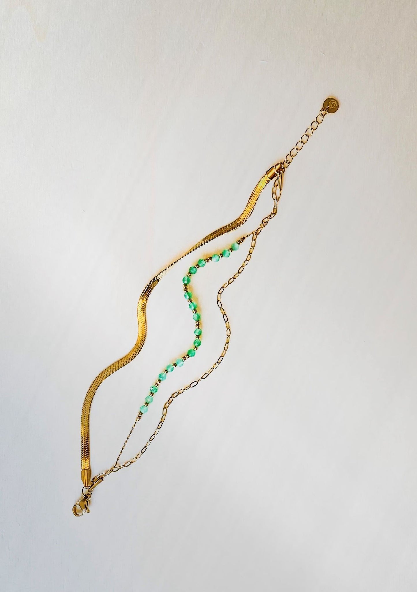 three tier bracelet with snake skin, green beads and chain element on plain white background.