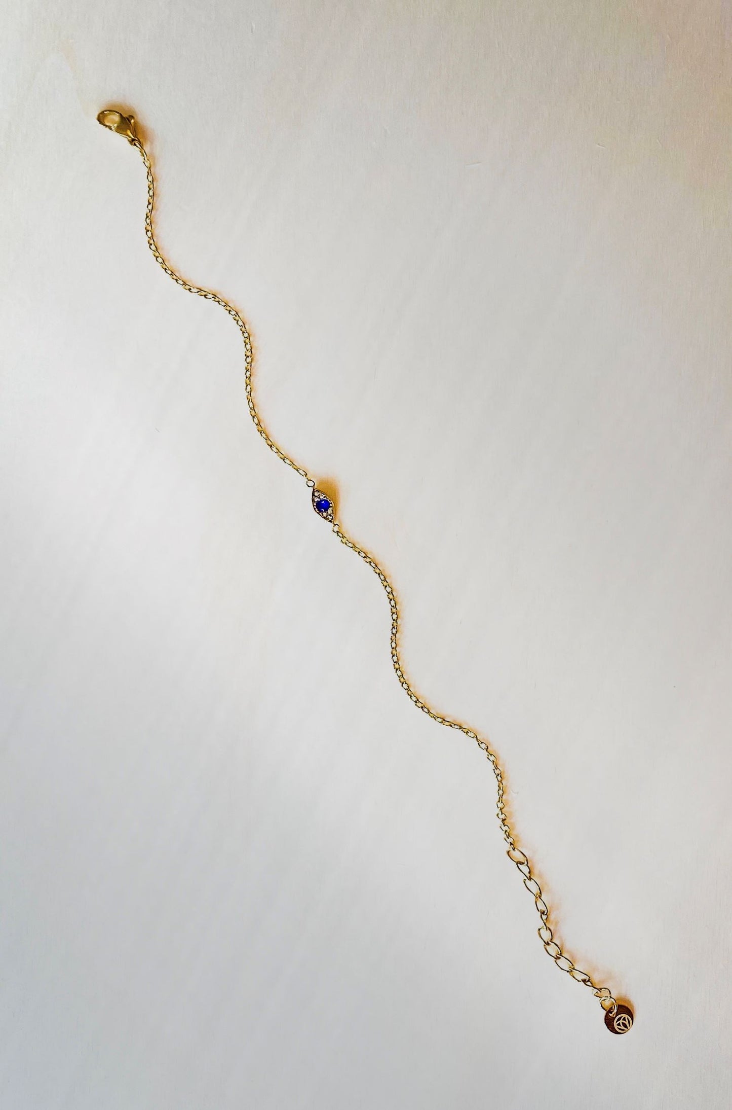 chain bracelet in gold with evil eye charm on plain beige background.