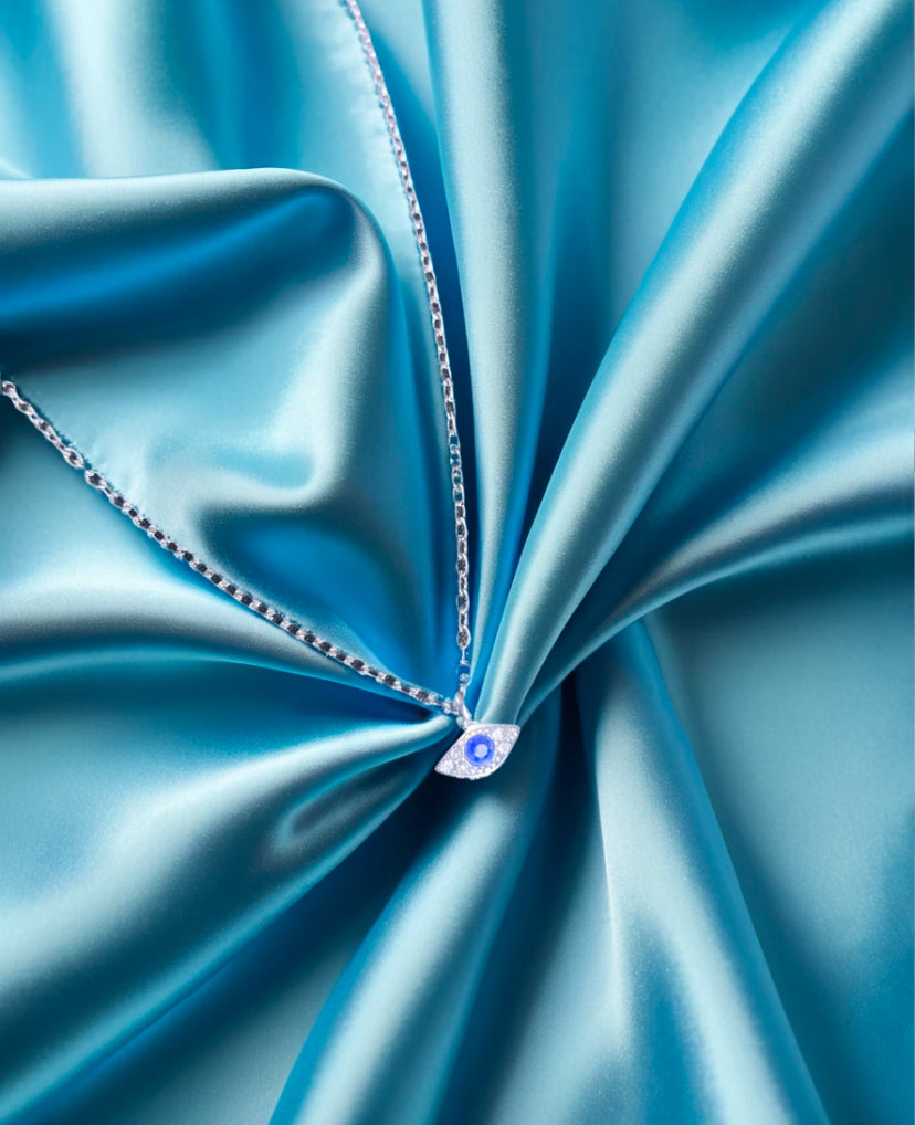 evil eye necklace in silver on blue silk background