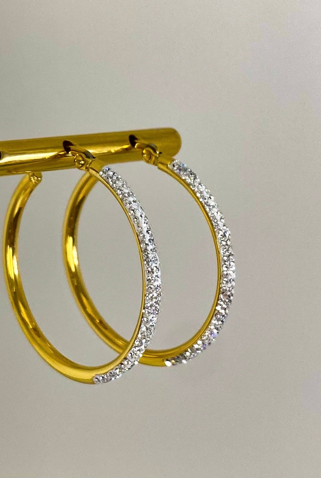 Gold plated Sparkling Hoop Earrings with diamond detail. Gold display and a beige background