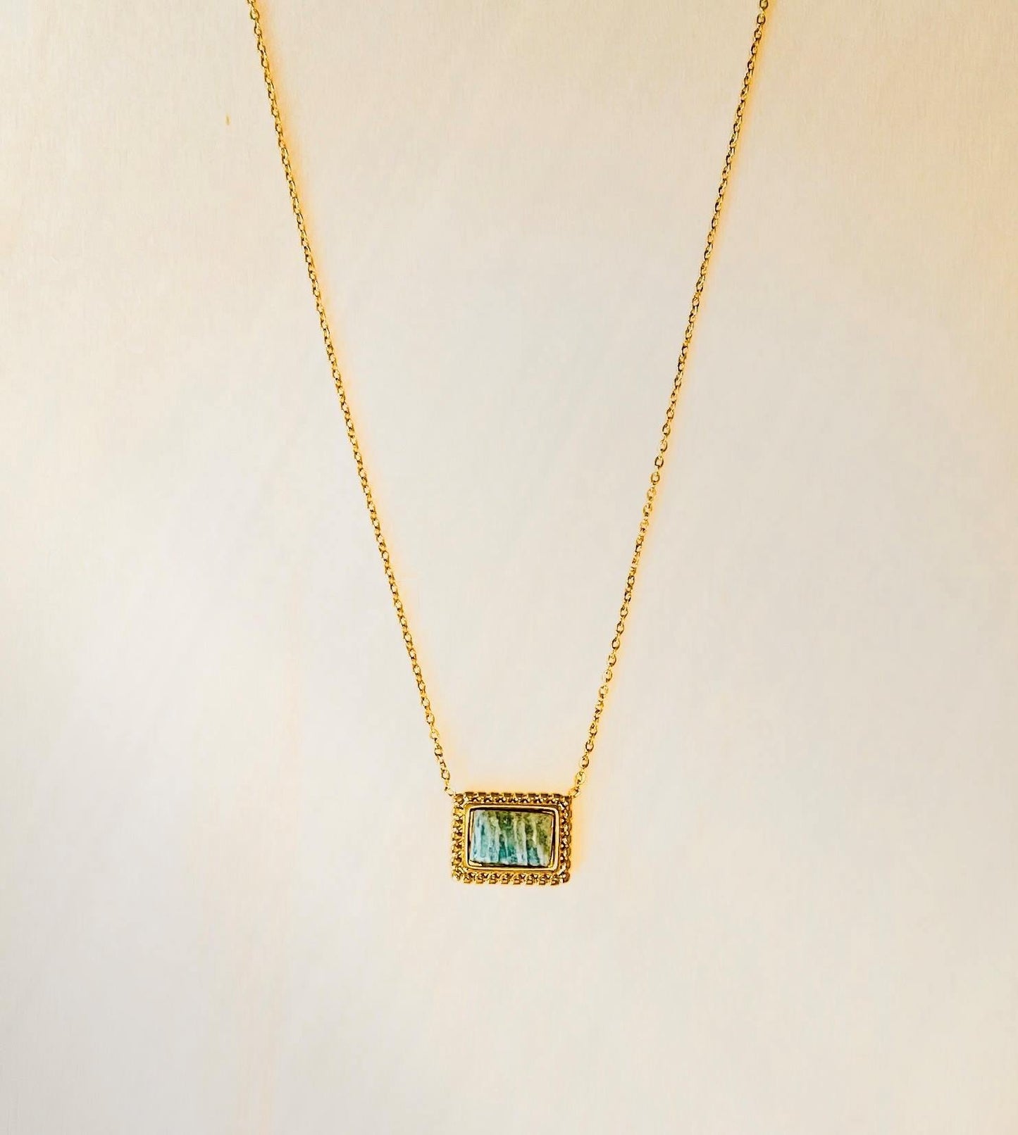 gold plated pendant necklace with green detailed stone on plain beige background