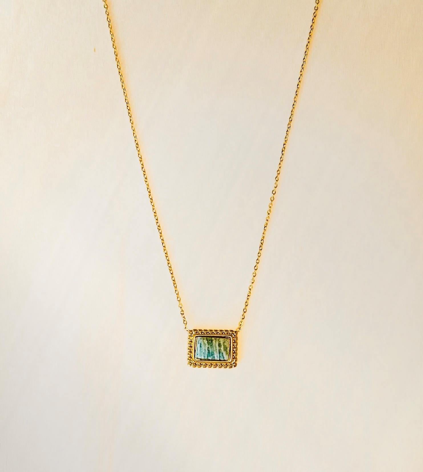 gold plated pendant necklace with green detailed stone on plain beige background