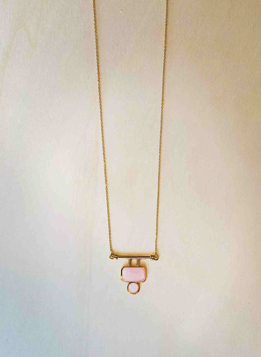 gold plated t-bar pendant necklace with pink stone on plain beige background.