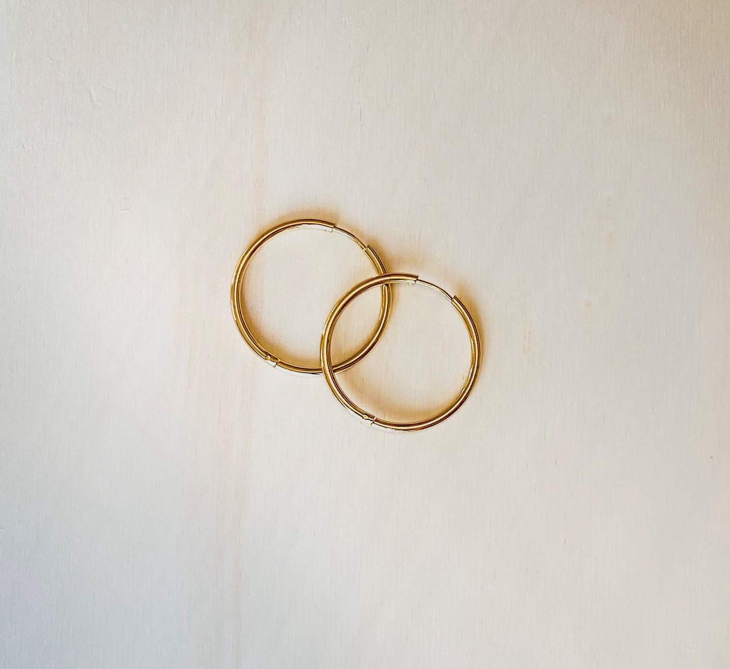 two gold-plated hoop earrings on plain beige background.