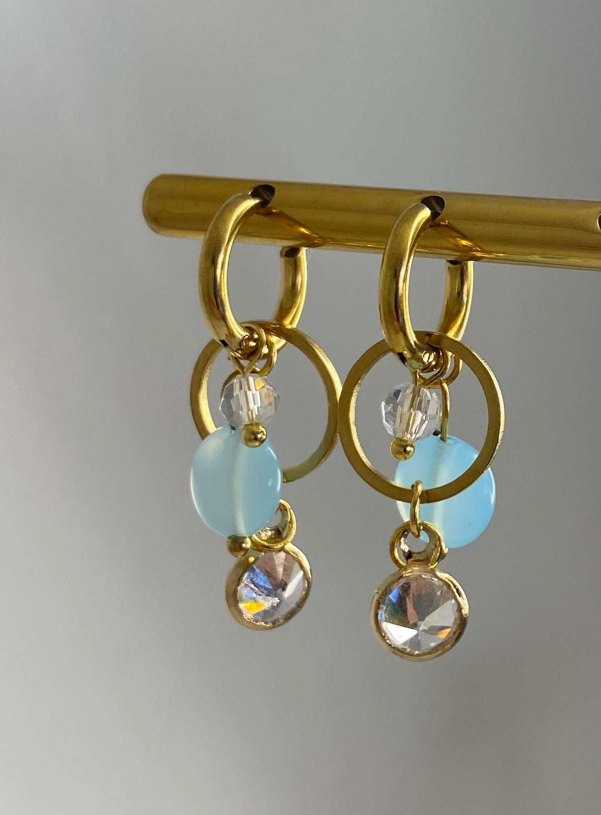 gold and blue drop earrings on gold display with white background. gold hoop drop earrings. chandelier earrings on gold display.