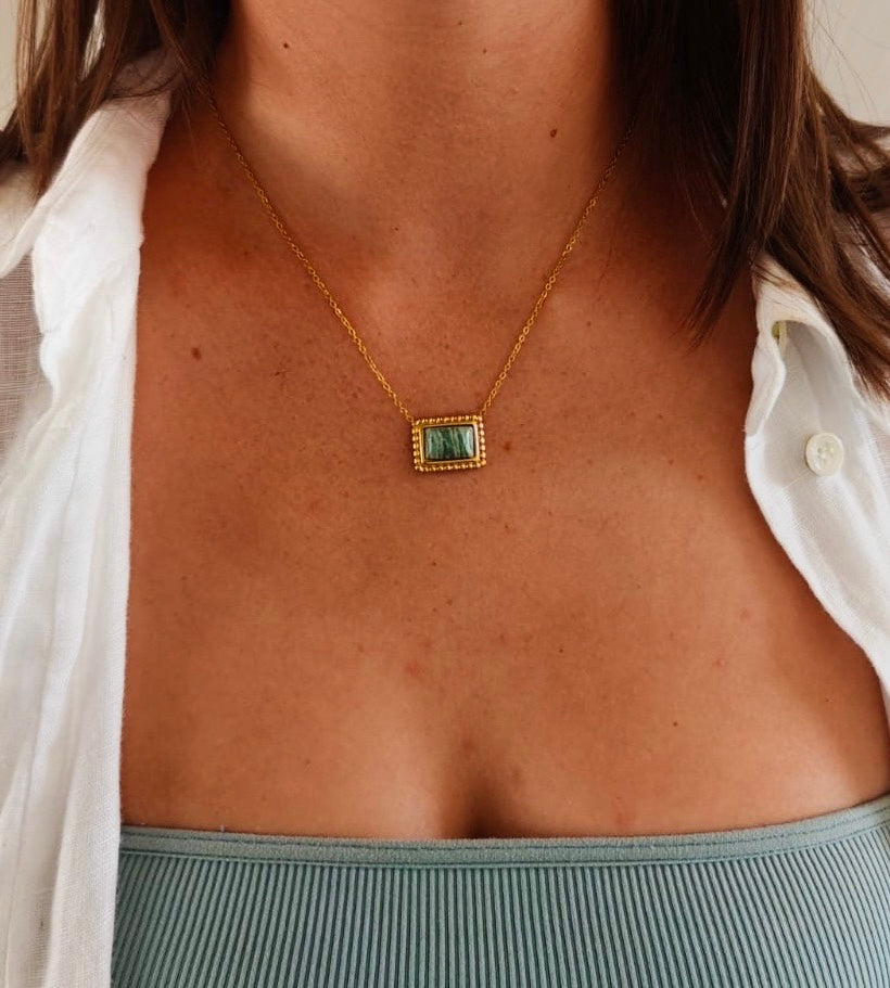 brunette model wearing a white shirt, blue top and gold pendant necklace with green stone.