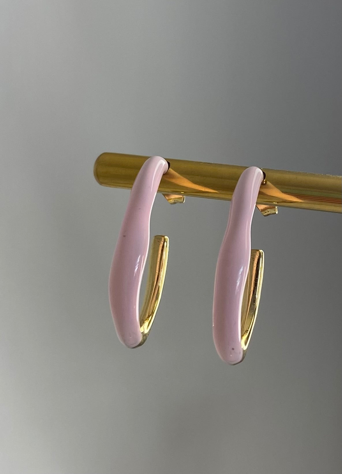 front profile of pink and gold enamel and stainless steel earrings on gold display white white background. 