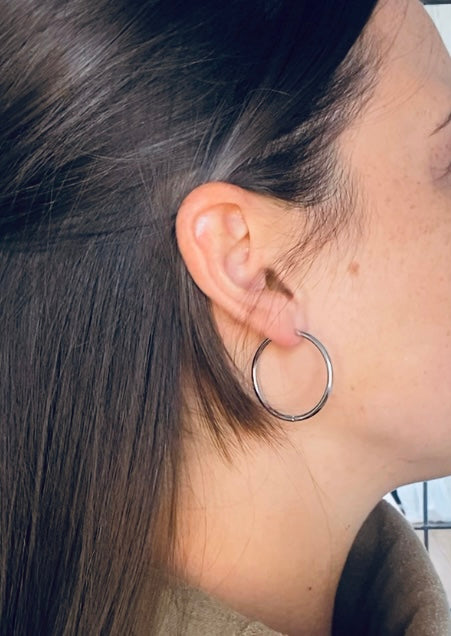 brunette woman with beauty mark modelling silver hoops earrings.