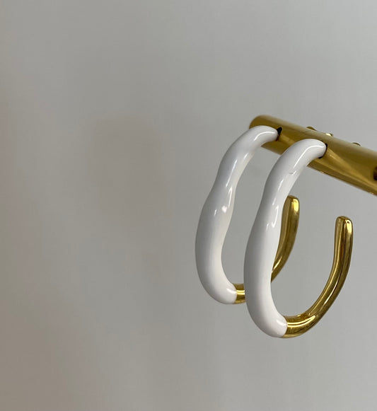 white and gold enamel and stainless steel earrings on gold display with white background. 