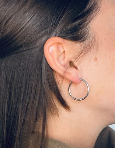 brunette woman with beauty mark modelling silver hoops earrings.